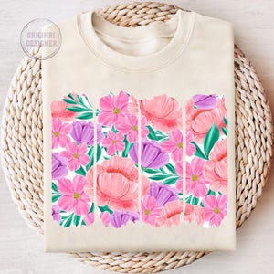 May include: A beige sweatshirt with a floral print design. The print features pink, purple, and green flowers.