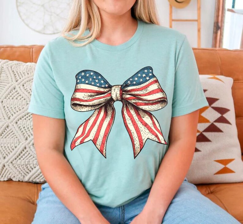 Peut inclure: Un t-shirt bleu clair avec un grand n&oelig;ud rouge, blanc et bleu imprim&eacute; sur le devant. Le n&oelig;ud est con&ccedil;u pour ressembler au drapeau am&eacute;ricain.