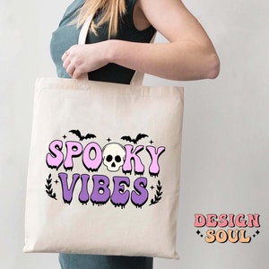 May include: A white tote bag with a pink and purple design that says "Spooky Vibes" with a skull and bats.