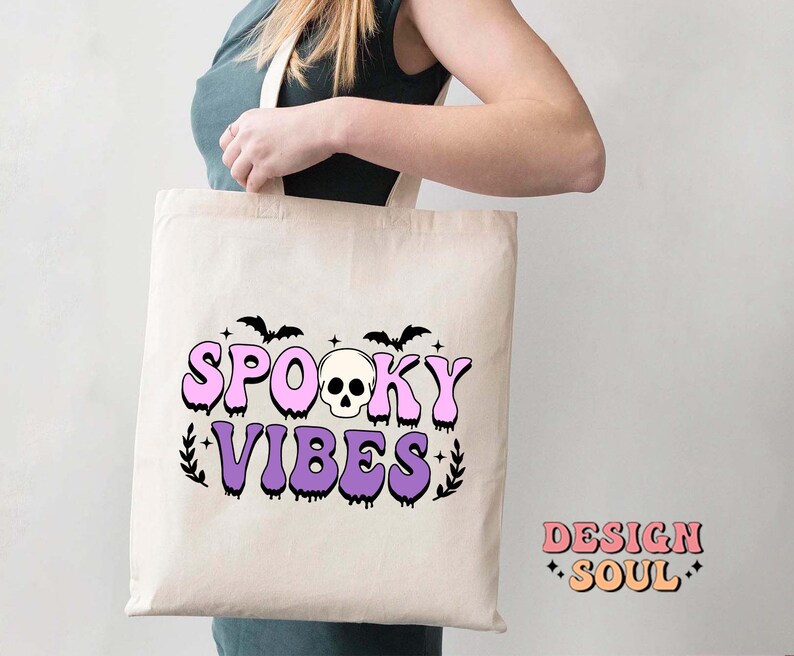 May include: A white tote bag with a pink and purple design that says "Spooky Vibes" with a skull and bats.