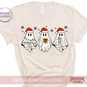 May include: A beige t-shirt with a digital download PNG graphic of three ghosts wearing Santa hats. The ghosts are holding gifts and a cup of coffee. The text "Design Soul" is in the bottom right corner.