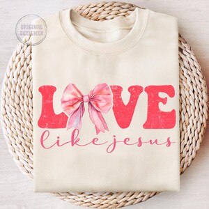 May include: A cream-coloured sweatshirt with the words "LOVE like jesus" in pink lettering. A pink bow is centred above the text.