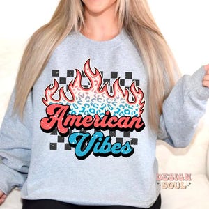 May include: A gray sweatshirt with a graphic of a red, blue, and white flame with a leopard print design. The text "American Vibes" is written in a retro font.