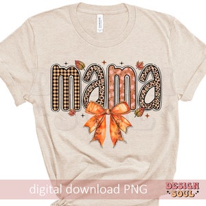 May include: A beige t-shirt with the word "mama" in a fall-themed design. The word is made up of different patterns, including plaid, leopard print, and floral. A large orange bow is below the word.