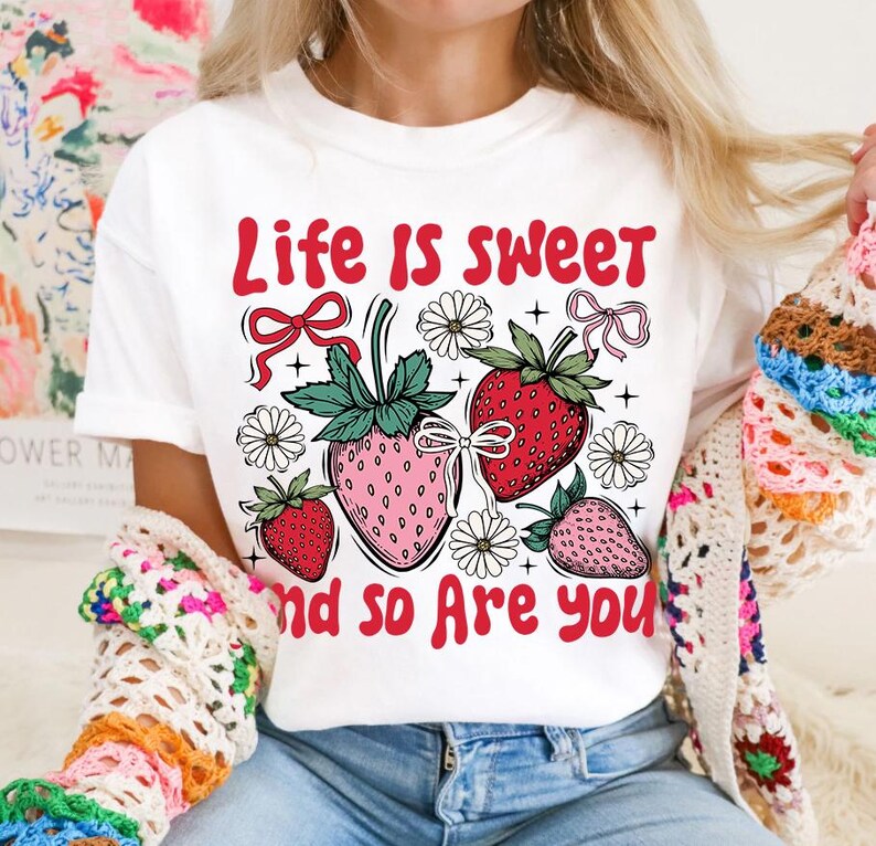May include: White t-shirt with a red graphic that says "Life is sweet and so are you". The graphic also features strawberries, flowers, and bows.