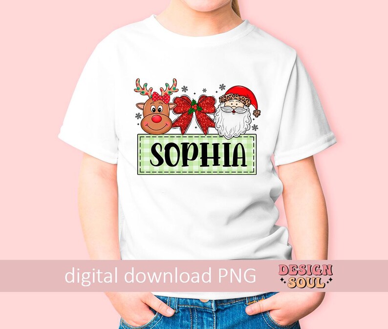 May include: White t-shirt with a green and white checkered box with the name "Sophia" in red letters. The box contains a cartoon reindeer with a red bow, a red bow, and a cartoon Santa Claus with a white beard.