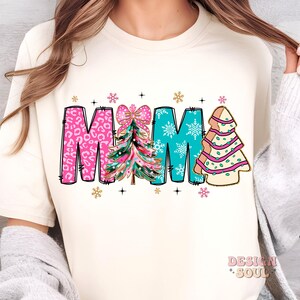 May include: A white t-shirt with the word "MAMA" in pink, blue, and gold letters. Each letter has a Christmas tree design with a pink bow on the "A".