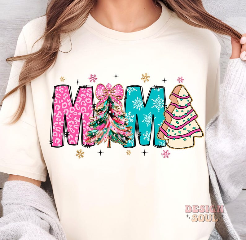 May include: A white t-shirt with the word "MAMA" in pink, blue, and gold letters. Each letter has a Christmas tree design with a pink bow on the "A".