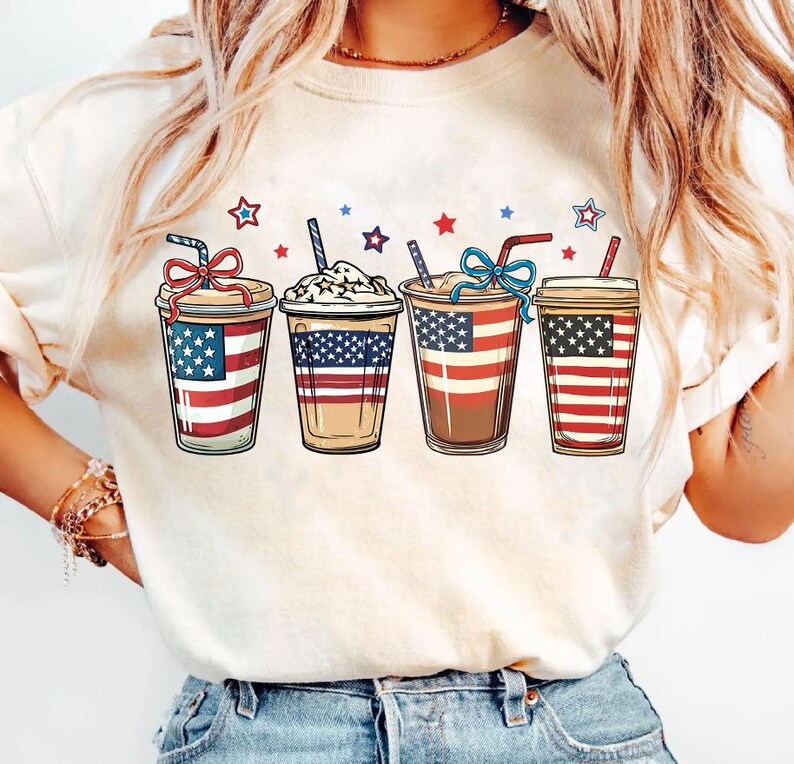 May include: White t-shirt with a graphic of four iced coffee drinks decorated with red, white, and blue stars and stripes.