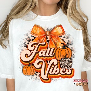 May include: White t-shirt with an orange and brown bow, pumpkins, and the text "Fall Vibes" in a retro font.