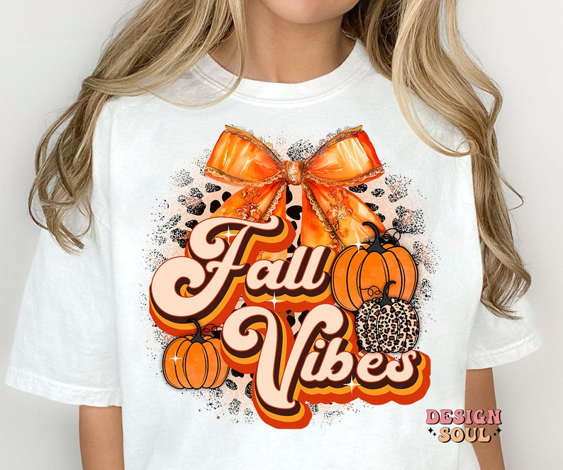May include: White t-shirt with an orange and brown bow, pumpkins, and the text "Fall Vibes" in a retro font.