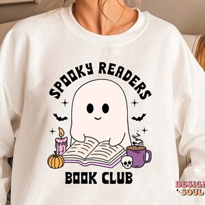 May include: White sweatshirt with a black and white illustration of a ghost reading a book. The text "Spooky Readers Book Club" is printed on the sweatshirt.