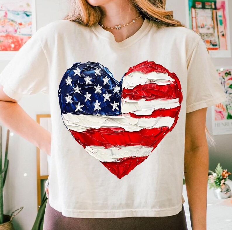 Pu&ograve; includere: Una maglietta bianca con un design a forma di cuore dipinto in rosso, bianco e blu. Il cuore &egrave; a forma di bandiera americana.