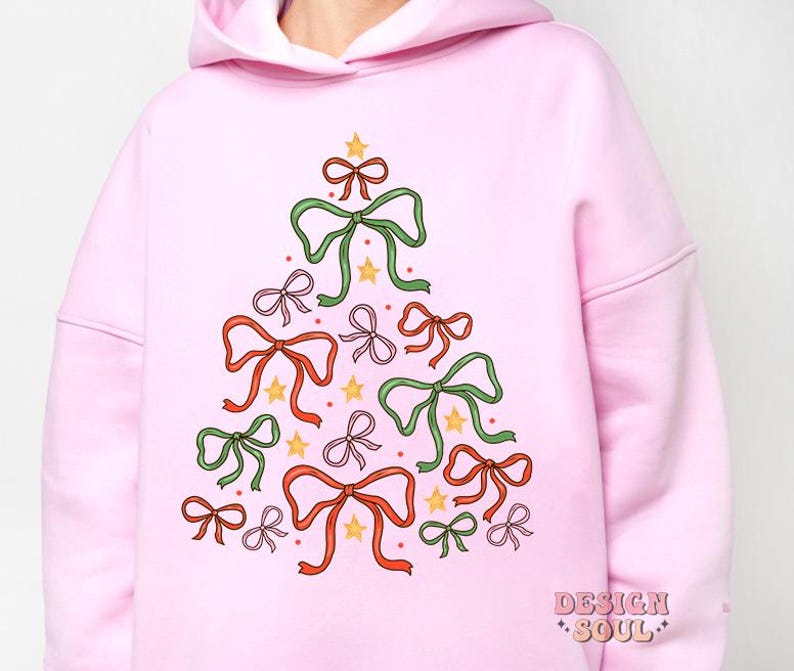 May include: Pink hoodie featuring a Christmas tree design made of bows in various colours, including green, red, pink, and yellow. The tree is decorated with gold stars.