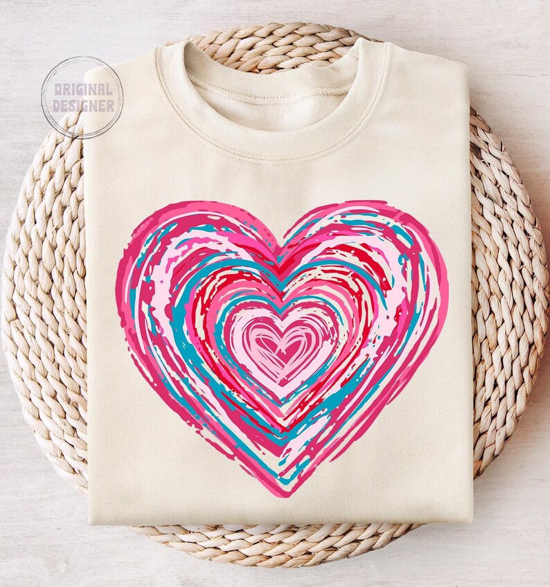 Pu&ograve; includere: Una felpa color crema con un grande disegno a forma di cuore rosa, rosso e blu. Il cuore &egrave; composto da cerchi concentrici di colore, con un cuore pi&ugrave; piccolo al centro.