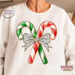 May include: White sweatshirt with a graphic of two candy canes tied together with a black and white polka dot bow. The candy canes are red and white and green and white.