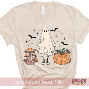 May include: A beige t-shirt with a ghost, mushrooms, and a pumpkin design. The ghost is white and has a friendly face. The mushrooms are orange and brown. The pumpkin is orange and has a green stem. The design is in a vintage style.