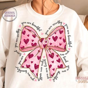 May include: White sweatshirt with a pink and gold bow with glitter and the text "you are beautiful you are worthy you are loved you are beautiful" repeated around the bow.