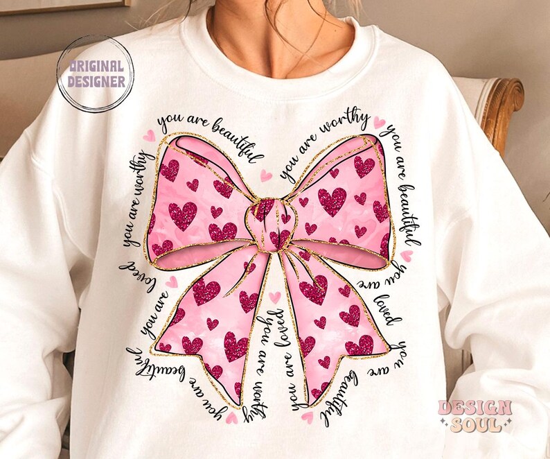 May include: White sweatshirt with a pink and gold bow with glitter and the text "you are beautiful you are worthy you are loved you are beautiful" repeated around the bow.
