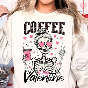 May include: White sweatshirt with a pink skeleton wearing heart-shaped sunglasses and holding a cup of coffee. The text "COFFEE is my VALENTINE" is printed on the shirt.