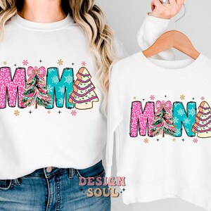 May include: White long-sleeve shirts with a Christmas tree design and the words "MAMA" and "MINA" in pink, blue, and green.