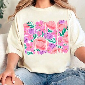 May include: A white t-shirt with a floral print featuring pink and purple flowers. The print is in a vertical stripe pattern.
