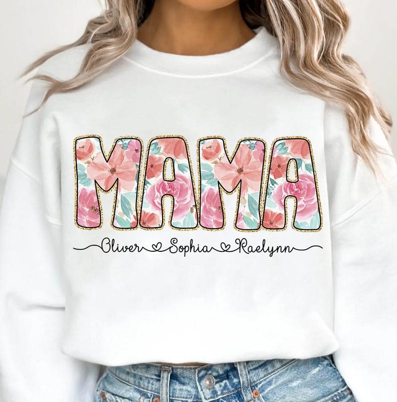 May include: White sweatshirt with the word "MAMA" in pink and peach floral letters. The names "Oliver", "Sophia", and "Raelynn" are written below the word "MAMA" in black.