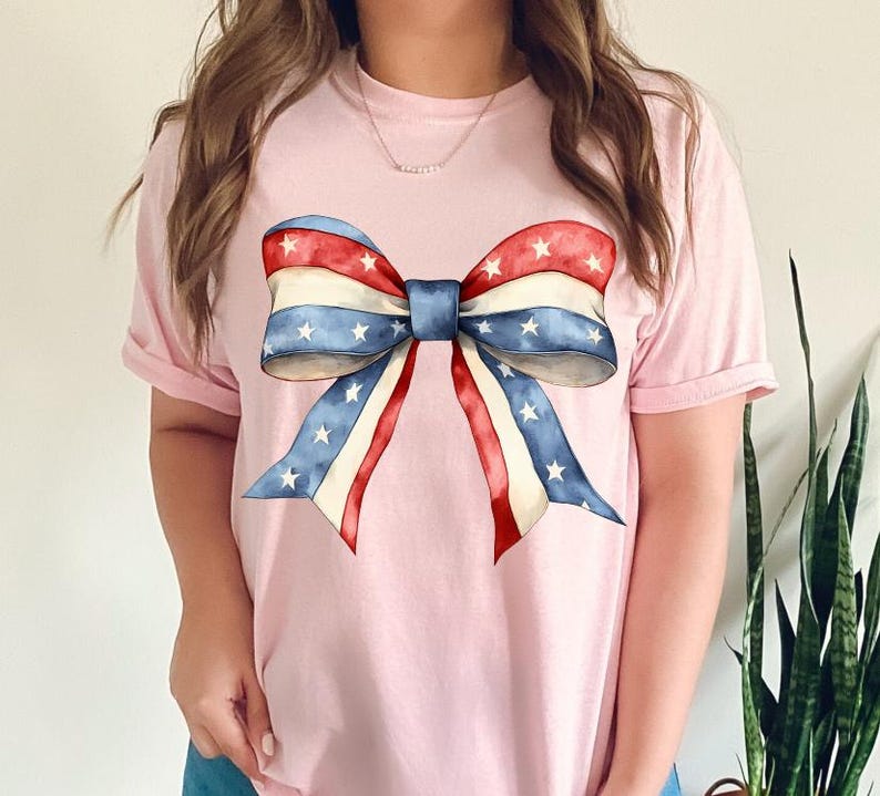 K&ouml;nnte beinhalten: Ein pinkfarbenes T-Shirt mit einer gro&szlig;en rot-wei&szlig;-blauen Schleife mit Sternen darauf.