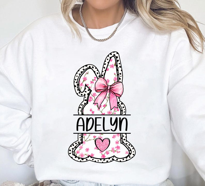 Pu&ograve; includere: Felpa bianca con un design di coniglio floreale rosa e il nome "Adelyn" stampato sotto. Il coniglio ha un fiocco rosa e un cuore rosa al centro.