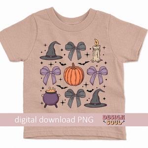 Puede incluir: Una camiseta marr&oacute;n claro con un dise&ntilde;o de tem&aacute;tica de Halloween. El dise&ntilde;o presenta una calabaza, un sombrero de bruja, una caldera, una vela y lazos en tonos de morado, gris y rosa.