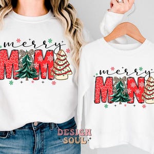 May include: White long-sleeved shirts with a Christmas-themed design. The larger shirt says "merry mama" with a red, green, and white design. The smaller shirt says "merry mina" with a similar design.