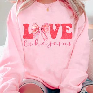 May include: Pink sweatshirt with a graphic design that says "LOVE like jesus" with a pink bow in the middle of the word LOVE.