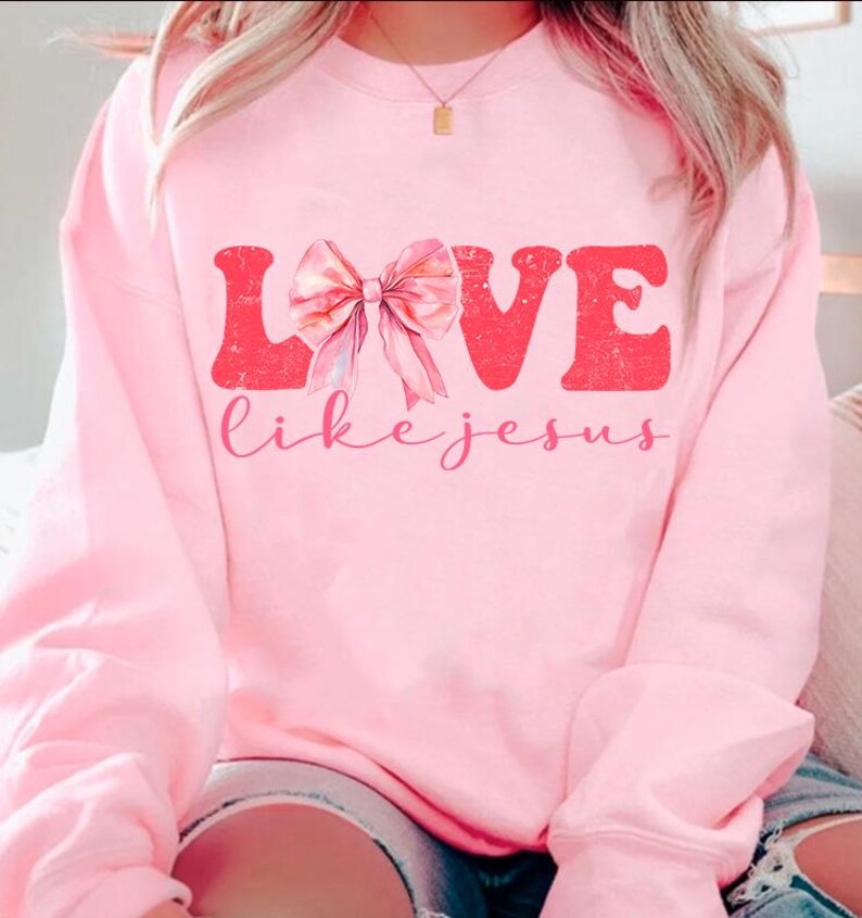 May include: Pink sweatshirt with a graphic design that says "LOVE like jesus" with a pink bow in the middle of the word LOVE.
