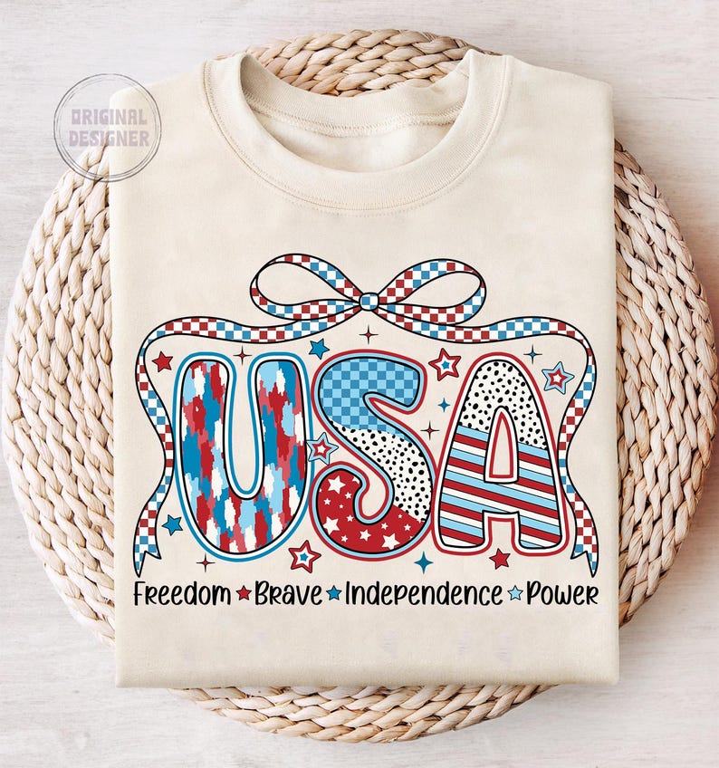 Peut inclure: Un sweat-shirt beige avec un graphique USA rouge, blanc et bleu. Le graphique est compos&eacute; d'&eacute;toiles, de rayures et de motifs &agrave; carreaux. Les mots "Freedom Brave Independence Power" sont imprim&eacute;s sous le graphique.