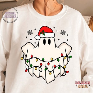May include: White sweatshirt with a cartoon ghost wearing a Santa hat and Christmas lights. The ghost has two black eyes and a red nose.