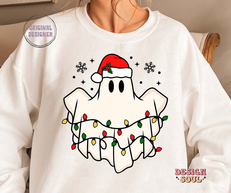 May include: White sweatshirt with a cartoon ghost wearing a Santa hat and Christmas lights. The ghost has two black eyes and a red nose.