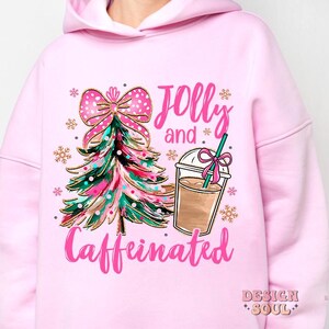 May include: Pink hoodie with a Christmas tree and a cup of coffee graphic. The text on the hoodie says "Jolly and Caffeinated".