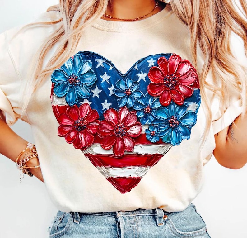 May include: A white t-shirt with a red, white, and blue heart-shaped design. The heart is made up of an American flag with red, white, and blue flowers painted around it.