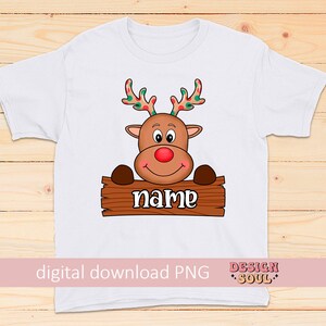 Peut inclure: T-shirt blanc avec un renne de dessin anim&eacute; tenant une pancarte qui dit "name". Le renne a des bois rouges avec des pois verts et blancs.