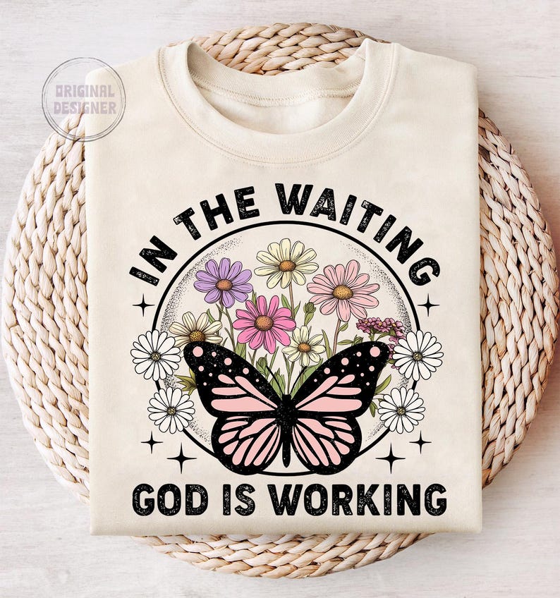 May include: A beige t-shirt with a black butterfly and floral design. The text "In the waiting God is working" is printed on the shirt.