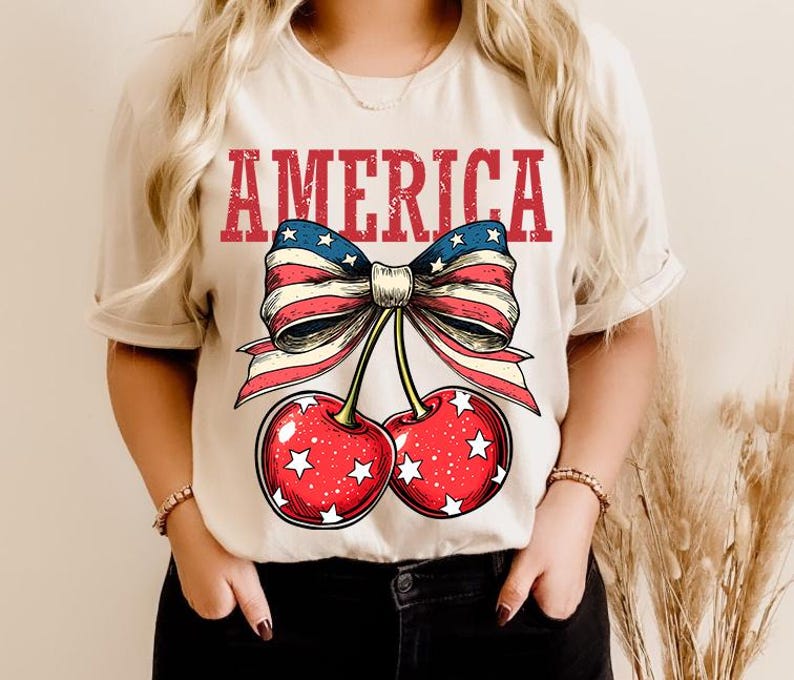 May include: A white t-shirt with a red, white, and blue bow with cherries and the word "AMERICA" printed on it.