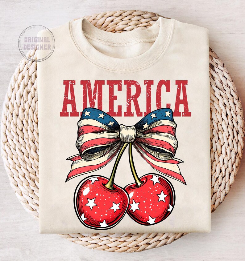 May include: A white t-shirt with the word "AMERICA" printed in red letters. A red, white, and blue bow with stars is tied around two red cherries with white stars.