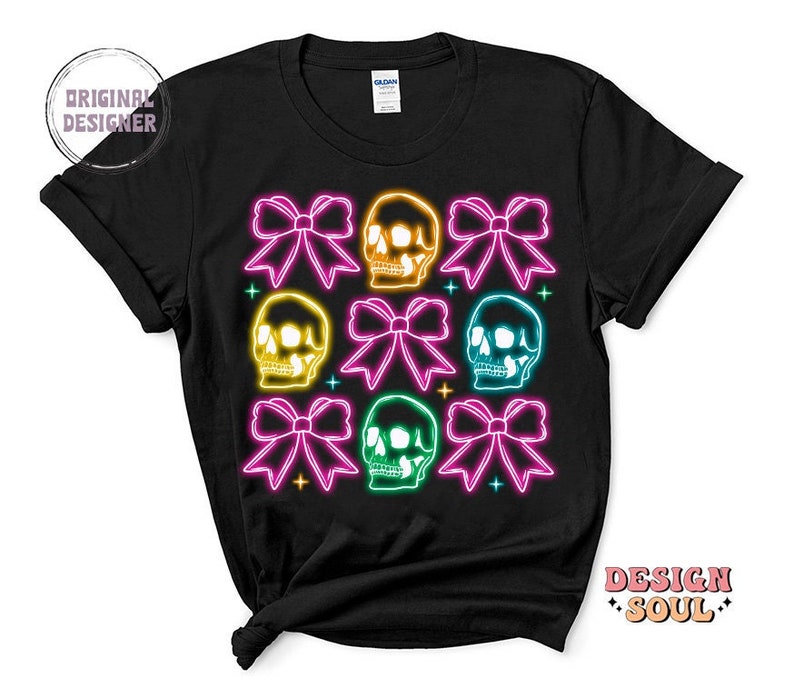 May include: Black t-shirt with a neon design of colorful skulls and bows. The skulls are outlined in neon yellow, green, pink, and blue. The bows are pink, yellow, and green.