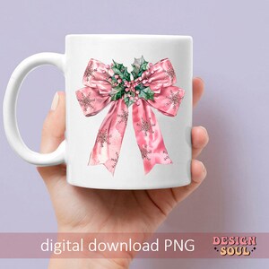 May include: A white ceramic mug with a pink bow and green holly design. The bow has a snowflake pattern and the holly has red berries.