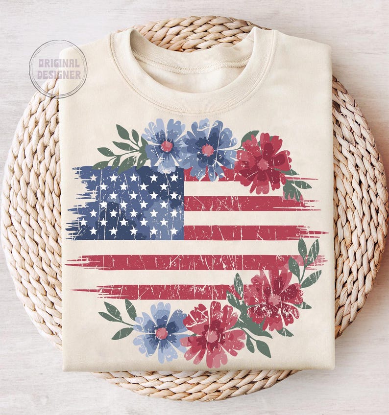 Puede incluir: Sudadera color crema con un dise&ntilde;o de bandera estadounidense desgastada con detalles florales rojos y azules. El dise&ntilde;o de la bandera incluye estrellas y rayas, con una corona floral alrededor de la bandera. El texto "ORIGINAL DESIGNER" es visible.