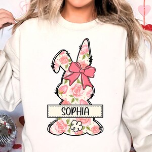 May include: White sweatshirt with a pink floral bunny design and the name "Sophia" printed below it.