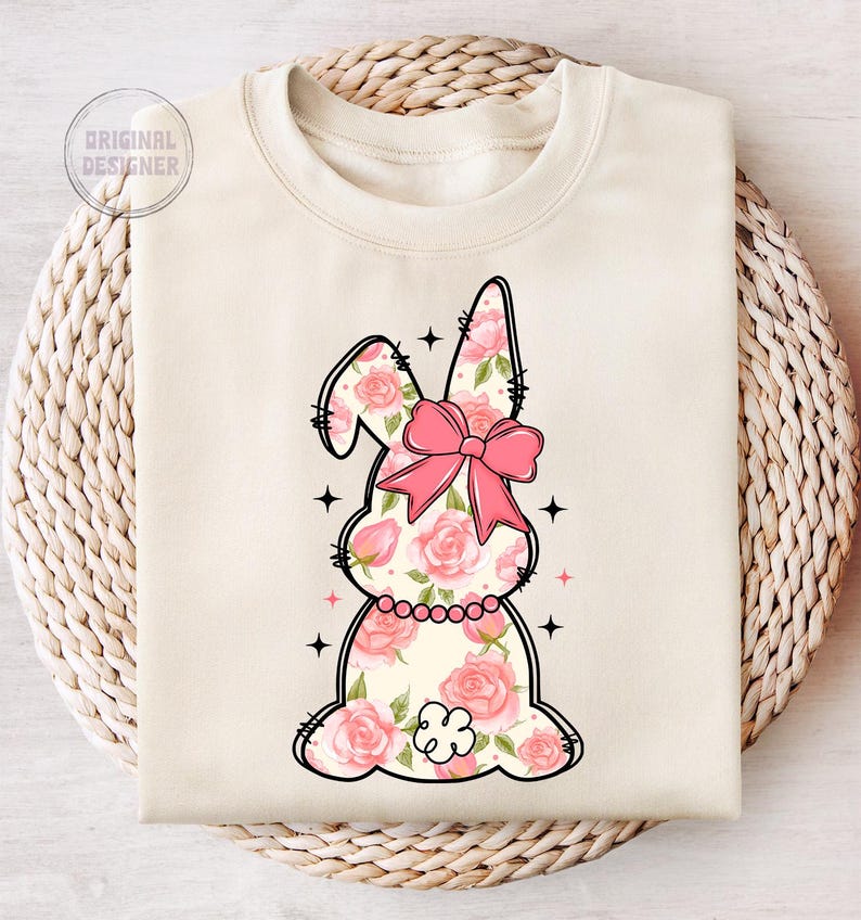 May include: A cream-colored sweatshirt with a floral bunny design. The bunny is pink and white with a pink bow. The bunny is surrounded by pink flowers.