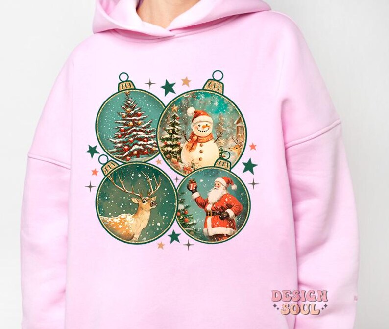 May include: Pink hoodie featuring a Christmas design with four ornaments depicting a snowman, reindeer, Santa Claus, and a Christmas tree. The ornaments are surrounded by stars.