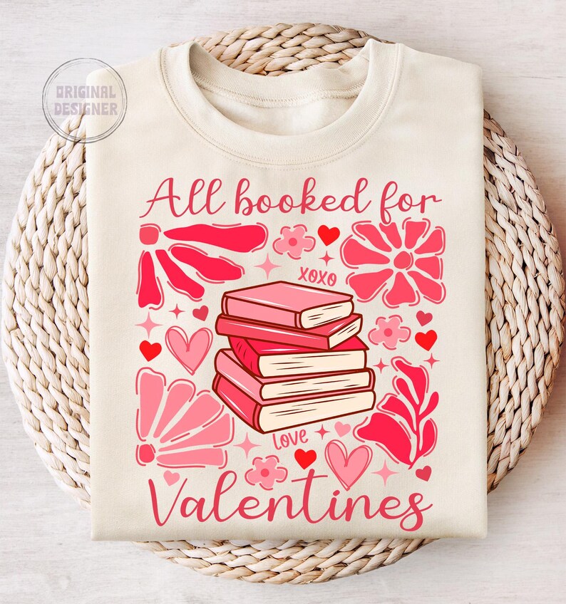May include: A cream-colored sweatshirt with the text "All booked for Valentines" in pink lettering. The design features a stack of pink books with the words "XOXO" and "Love" on them, surrounded by pink flowers and hearts.