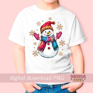 May include: A white t-shirt with a colorful snowman design. The snowman is wearing a red hat, a pink and purple scarf, and has a carrot nose. The design is surrounded by gold glitter snowflakes.